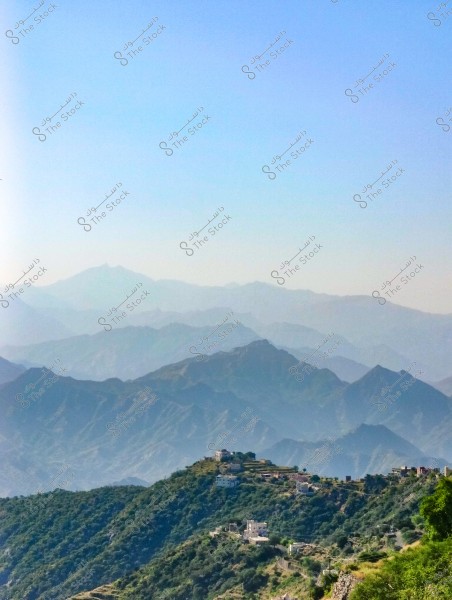 A landscape view of the terraced green mountains in the Asir region, Saudi Arabia. Hills covered with vegetation and scattered houses are visible on the mountain tops in the foreground, while multiple mountain ranges appear in the background under a clear blue sky.