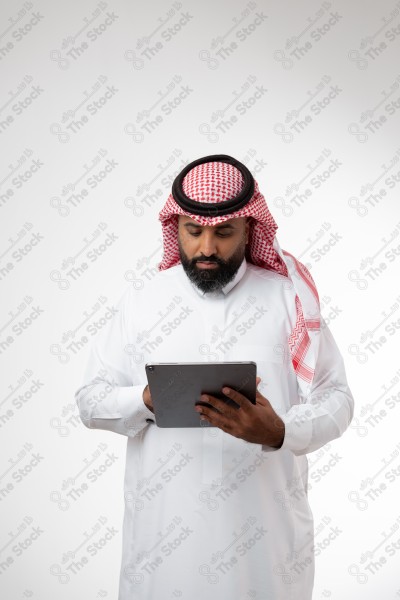 بورتريه رجل سعودي يحمل بيده الآيباد و ينظر لشاشته ويقوم بتعابير مختلفة، خلفية بيضاء