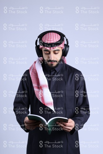 رجل سعودي يرتدي سماعة الرأس ويقرأ الكتاب.