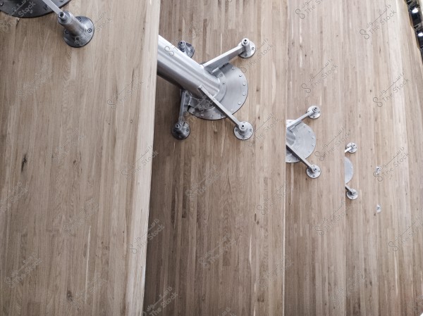 The image shows a metallic structure mounted on a prominent wooden surface. The surface features vertical wooden panels, while a horizontal metal beam with circular bases and support arms is attached to it.