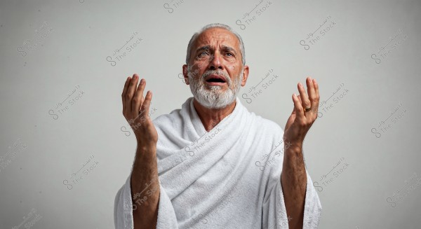 A portrait of a man with a white beard wearing white Ihram clothing, raising his hands in a praying position. His facial expressions convey deep emotions with tears on his cheeks. The background is simple and neutral.