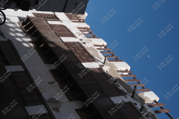 An image of an old traditional building façade with wooden brackets and decorative wooden windows, set against a calm blue sky with a half moon visible in the upper right corner.