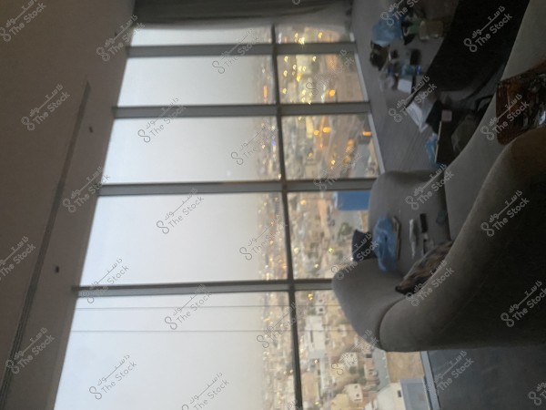 A view from inside a room with chairs and furniture, showcasing a cityscape at night through large glass windows. The city lights and buildings appear slightly blurry, creating a calm ambiance.