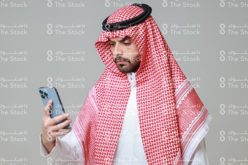 شاب سعودي يرتدي الزي السعودي التقليدي يستخدم الجوال، رجل يتصفح هاتفه المحمول