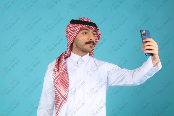 بورتريه رجل سعودي على خلفية تركوازي، يلتقط صورة شخصية (سيلفي) ، الاتصالات والتقنية.