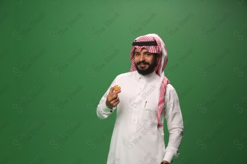 شاب سعودي على خلفية خضراء يرتدي الثوب و الشماغ، يقوم بعمل حركات بيده، يأكل الكعكة ، احتفالات العيد