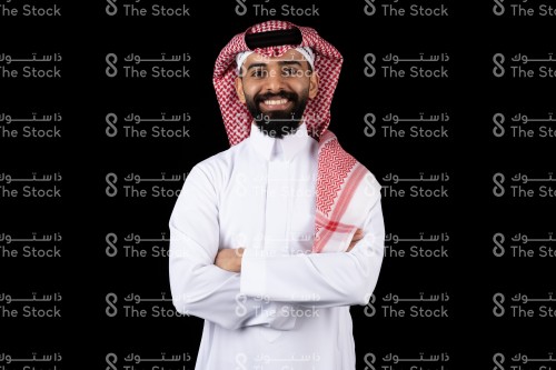 بورتريه رجل سعودي  يرتدي الثوب يقف على خلفية سوداء ينظر إلى الكاميرا وهو مبتسم