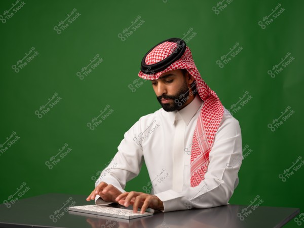 A man in traditional Gulf attire typing on a keyboard in front of a green background.
