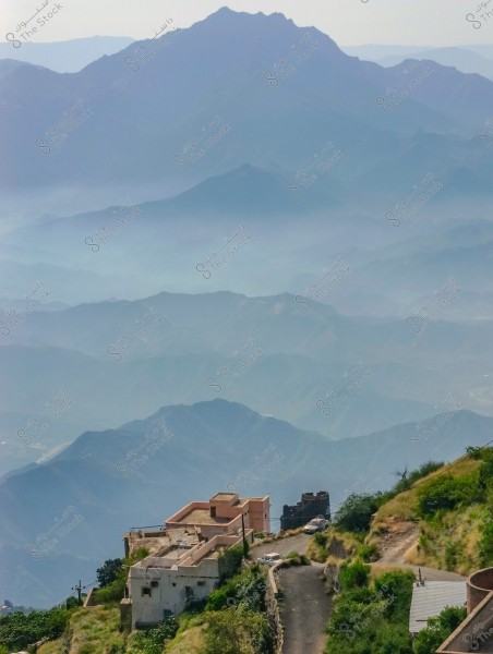 The image shows a natural landscape of various mountains enveloped in light mist, creating a layered effect of ascending hills. In the foreground, there is a quiet road alongside white buildings perched on a mountain peak. The colors range from green to bluish-gray under soft daylight.