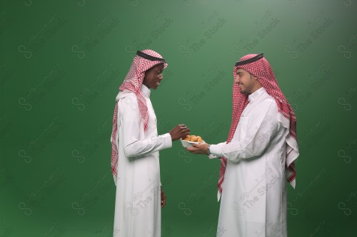 رجل سعودي يرتدي الثوب و الشماغ يقوم بتقديم الحلوى لرجل سعودي اخر