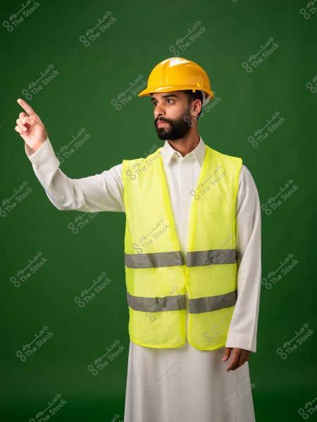 شخص يرتدي خوذة أمان صفراء وسترة عاكسة صفراء يشير بيده إلى الأعلى على خلفية خضراء.