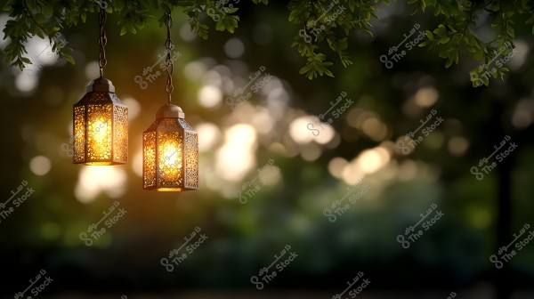 Two illuminated lanterns with intricate designs hanging from a tree with green leaves, soft sunset-like light appears in the background in a garden setting.