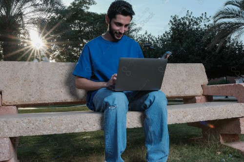 A Saudi man sits on a sofa in a public park and uses a mobile device during the day.