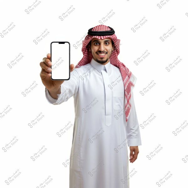 A portrait of a man wearing a thobe, ghutra, and agal, holding a smartphone with a blank screen, and smiling. The background is white, highlighting the traditional clothing, indicative of Saudi attire.