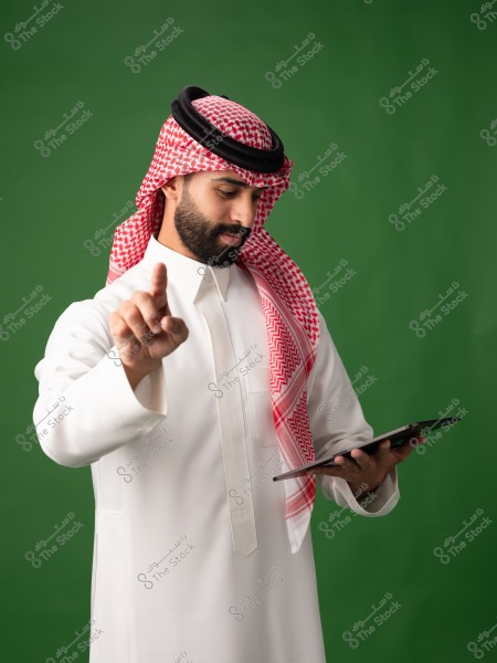 صورة لرجل يرتدي الثوب السعودي التقليدي, يتضمن غترة بيضاء وحمراء مع عقال أسود. يقف الرجل أمام خلفية خضراء, ممسكاً بجهاز لوحي في يده اليسرى, ويشير بسبابته اليمنى لأعلى.