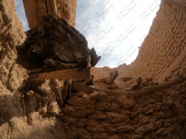 View of a partially collapsed roof of an old mud house showing a decayed wooden beam and natural light from the blue sky.