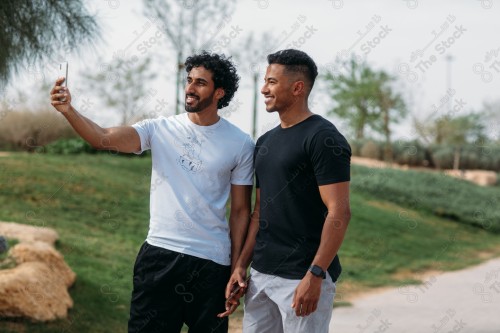 Two Saudi men chatting on a mobile phone during morning exercise in the open air, walking.