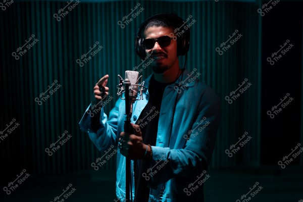 رجل يرتدي سماعات رأس ونظارات شمسية يقف أمام ميكروفون في استوديو.