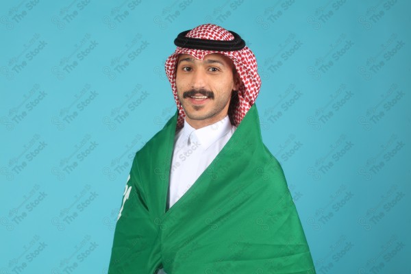 A young Saudi man wearing the Saudi dress and holding the Saudi flag makes expressions of happiness and enthusiasm, Saudi flag