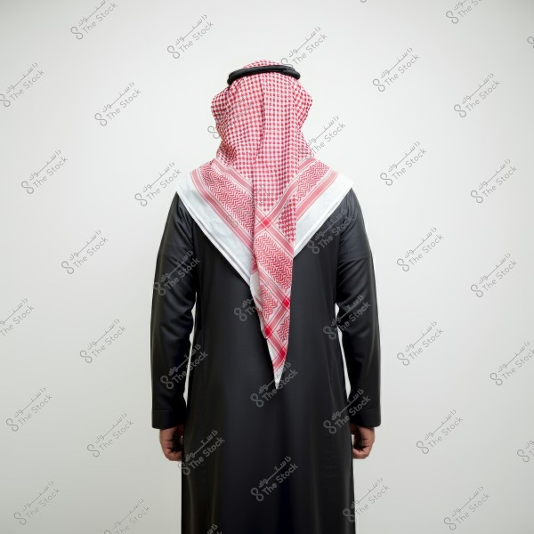 An image showing the back of a man wearing traditional Saudi clothing, featuring a black thobe and a red and white checkered keffiyeh on his head, representing traditional male attire in Saudi Arabia.
