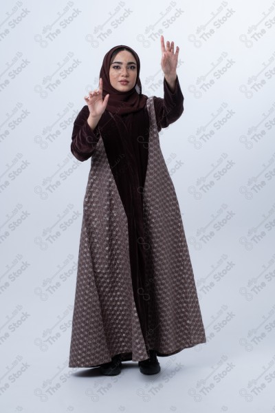 A young Saudi woman wearing an abaya and pointing with her finger. Standing on white background.