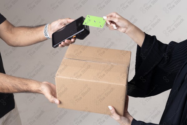 Portrait of a Saudi woman holding a card and making automatic payments, with a cardboard next to her on a white background