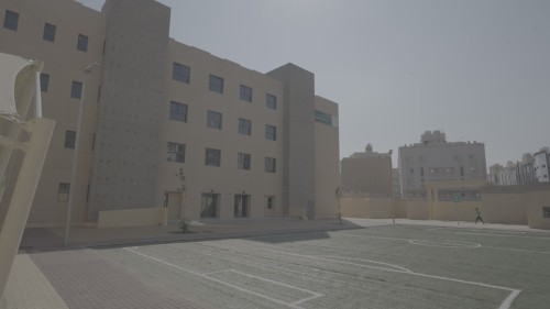 مبنى حديث به ملاعب رياضية في الخارج، مع وجود شخص يمشي في الفناء تحت أشعة الشمس الساطعة.