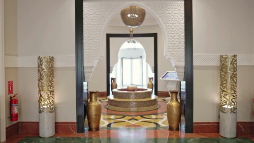 Video showcasing interior views of a lobby decorated with luxurious Arabic architectural design inside a hotel in Riyadh. The video features a central fountain surrounded by beautiful details such as ornate wall patterns and large bronze vases, with a digital screen for media display.