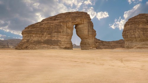 فيديو يعرض مشاهد من صخرة الفيل الشهيرة في العلا, السعودية, تحت سماء زرقاء تتخللها غيوم متفرقة, ما يبرز جمال التكوينات الصخرية الطبيعية في المنطقة الصحراوية.