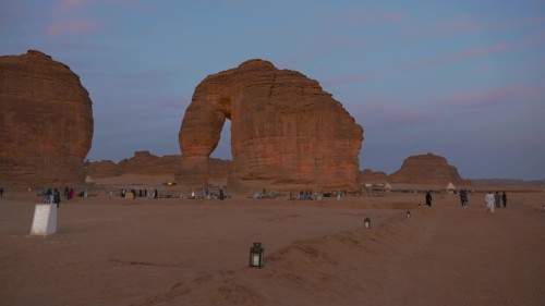 مشاهد من الفيديو تظهر صخرة الفيل الشهيرة في منطقة العلا بالمملكة العربية السعودية, مع وجود أشخاص يتجولون في المنطقة في وقت الغروب, حيث يتيح المشهد الجوي رؤية واضحة للتكوينات الجيولوجية البارزة وأجواء المهرجانات والأنشطة الثقافية في الموقع.