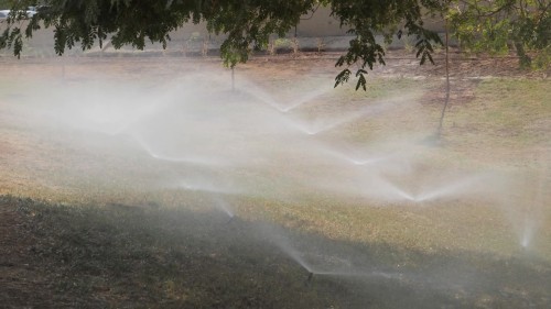 The video shows an irrigation system watering the grass in a garden, with water flowing evenly from ground-mounted sprinklers to cover the area fully.