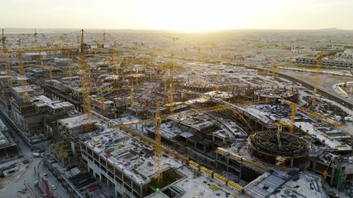 Aerial shots of a massive construction site showing numerous cranes and intensive construction work at various stages of development with the sunset in the background.