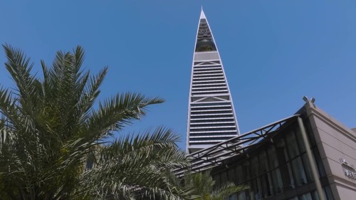 مشاهد جوية لمدينة الرياض تُظهر معالم معمارية حديثة مثل برج الفيصلية ووسط المدينة النابض بالحياة مع حركة المرور وتخطيط حضري متطور.