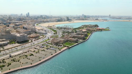 مشهد جوي لمدينة جدة تتميز بمباني مرتفعة, وشوارع فسيحة محاطة بالأشجار والحدائق, تلتقي بالواجهة البحرية الزرقاء.