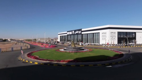 Video showcasing the New Mas Center, a modern and large building with a sleek glass design. The site features a decorated fountain and a golden sculpture in the center of a roundabout. The scene depicts a sunny day with cars parked along the side of the road.\r\n\r\n-
