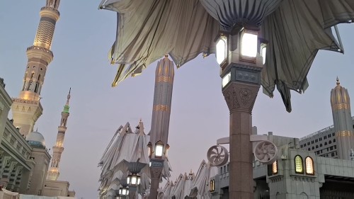 A video showcasing views of the Prophet\'s Mosque in Medina, featuring large umbrellas and magnificent minarets under the sunset sky, adding beauty and grandeur to this spiritual and historical site.