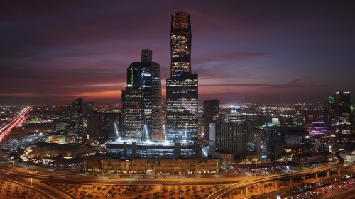منظر جوي لبنايات ناطحات السحاب في مدينة الرياض ليلاً, تُظهِر تفاصيل المعمار الحديث والأضواء الباهرة التي تُزيّن المدينة تحت سماء ملونة بألوان الغروب.\r\n\r\n-