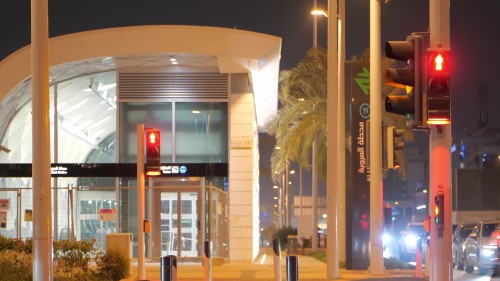 يظهر الفيديو محطة مترو \"العروبة\" في الليل, مع سيارات تعبر إشارة مرور حمراء مضاءة للمشاة والسيارات. الأشجار والنخيل تزين الطريق بجانب المحطة, والإضاءة الليلية تضفي جواً هادئاً في المشهد الحضري.\r\n\r\n-
