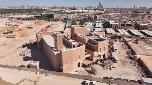 The video captures aerial views of a cultural heritage complex under construction in an urban area, featuring traditional architectural designs and distinct heritage elements. The scene highlights the mud-walled buildings and traditional towers in the foreground, surrounded by open spaces, development facilities, and the city skyline in the background.\r\n\r\n-