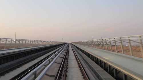 A video showcasing a train journey on a modern railway track extending through a vast desert area with an open landscape at sunset, focusing on the railway track and surrounding lighting.\r\n\r\n-