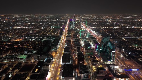 لقطات جوية لمدينة الرياض مضاءة بأضواء الليل, تُظهر الشوارع المكتظة بالأضواء والمباني المتلألئة بالأنوار الساطعة, مما يظهر حيوية المدينة وازدهارها ليلاً.