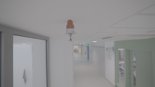 The video showcases a modern-designed corridor in an institutional or office building, featuring a fire sprinkler system on the ceiling along with air conditioning and lighting systems. The corridor is characterized by simplicity and predominant white color, with glass details seen in the windows and doors.